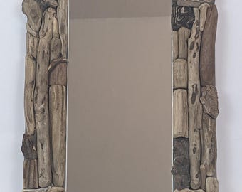 Peut inclure: Miroir rectangulaire avec un cadre composé de divers morceaux de bois flotté dans des tons bruns et gris. Les morceaux de bois flotté sont disposés pour créer une esthétique rustique et naturelle. La surface réfléchissante du miroir est visible.