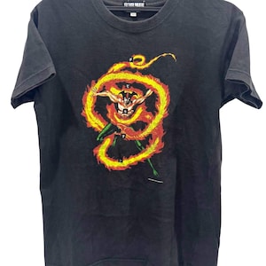 May include: A black short-sleeve t-shirt featuring a graphic print of a character surrounded by a swirling orange and yellow flame design. The shirt includes Japanese text characters within the flames and the word DEVILMAN on the inner neck label.