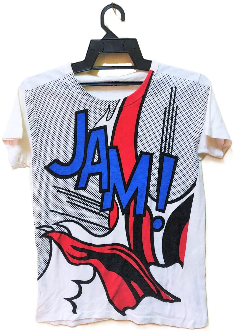 Puede incluir: Camiseta blanca con un gr&aacute;fico estilo c&oacute;mic. El dise&ntilde;o presenta la palabra "JAM!" en letras azules con contornos negros, sobre un estallido rojo y negro. El fondo tiene un patr&oacute;n de puntos.