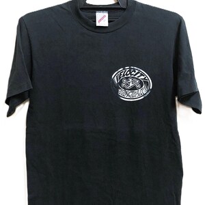 Op de afbeelding: Zwart T-shirt met een witte afbeelding. De afbeelding is een cirkelvormig ontwerp met het woord "VELOCITY" en een gestileerde surfer. Het shirt hangt aan een zwarte hanger.