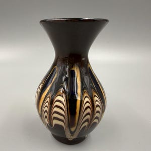 May include: A dark brown ceramic vase with a flared top and a bulbous body. The vase features a decorative pattern of wavy lines in cream and gold against a dark brown background. The vase is approximately 7 inches tall.