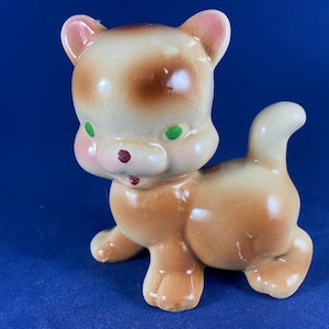 May include: A ceramic figurine of a brown and white cat with green eyes. The cat is standing on all fours and has a playful expression.