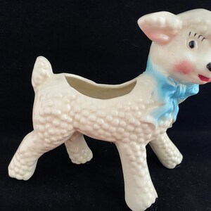 May include: White ceramic lamb planter with a blue bow. The lamb has a textured surface and a small opening on its back for planting.