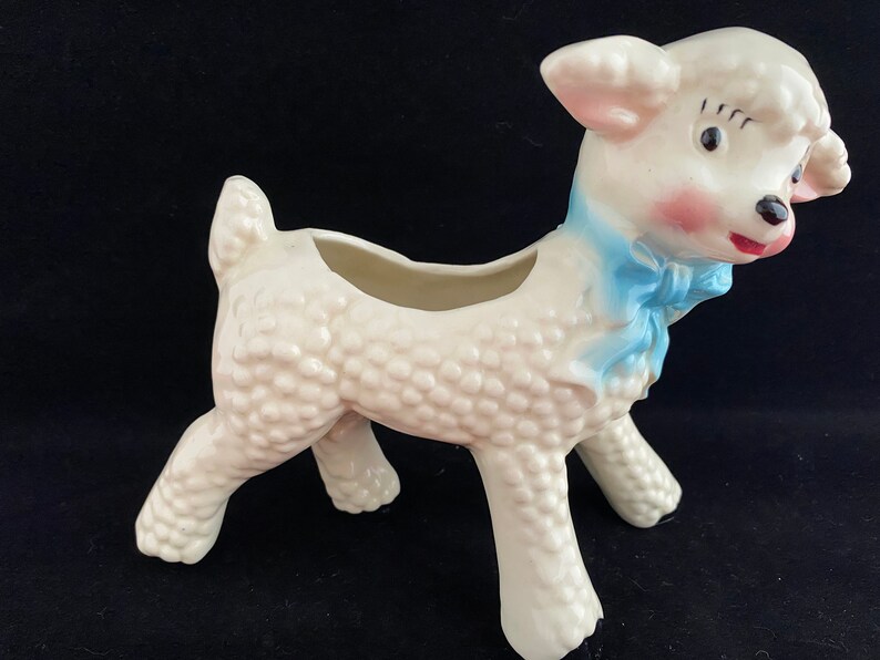 May include: White ceramic lamb planter with a blue bow. The lamb has a textured surface and a small opening on its back for planting.