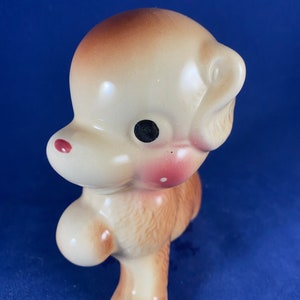 May include: A ceramic figurine of a brown and white dog with black eyes and pink accents. The dog is standing on its hind legs with its front paws raised.