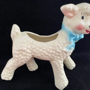 May include: White ceramic lamb planter with a blue bow. The lamb has a textured surface and a small opening on its back for planting.