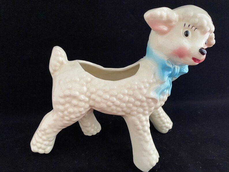 May include: White ceramic lamb planter with a blue bow. The lamb has a textured surface and a small opening on its back for planting.