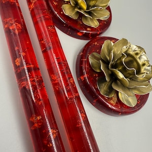 May include: Close-up of two red, transparent candle holders with gold flecks, and two red, round candle holders with gold flower-shaped candle holders. The candle holders are on a white surface.