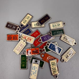 May include: A collection of vintage Illinois license plate keychains. Each keychain features a rectangular metal plate with embossed numbers and text, including "Land of Lincoln." The keychains are in various colors, including red, green, and blue.