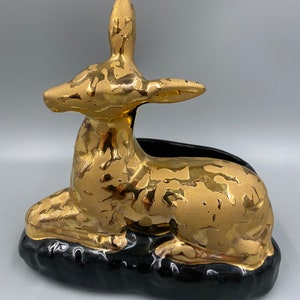May include: Gold ceramic deer planter with black base. The deer is sitting on a black base and has a gold glaze with a marbled effect.