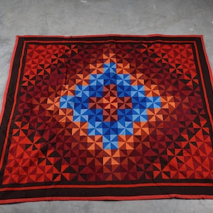 May include: A red, orange, and blue geometric patterned quilt with a dark brown border.