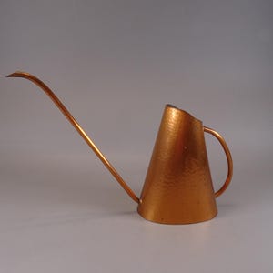 Op de afbeelding: Een koperen gieter met een gehamerde afwerking en een lange, gebogen tuit.