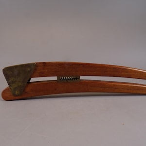 Pode incluir: Um espremedor de alho de madeira com uma placa de latão na parte superior. O espremedor de alho é feito de duas peças de madeira que são articuladas.