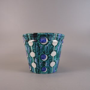 Peut inclure: Un pot en céramique blanche avec un motif géométrique vert et bleu. Le motif présente des cercles blancs avec des cercles bleus à l'intérieur, reliés par de fines lignes vertes.