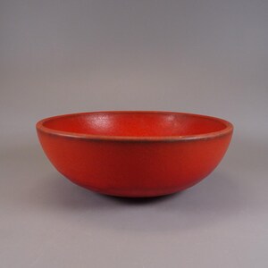 May include: A vibrant red bowl with a rounded shape. The bowl has a smooth, matte finish and a slightly darker rim. The interior of the bowl is a solid, bright red color. The bowl is likely made of ceramic or a similar material.