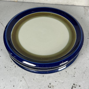 Può includere: Una pila di due piatti rotondi in ceramica caratterizzati da un bordo esterno blu profondo lucido, un'ampia fascia verde oliva al centro e un interno circolare liscio color beige chiaro. I piatti presentano un design semplice con finitura smaltata.