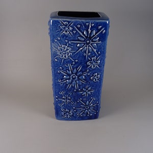 Peut inclure: Un vase en céramique bleu de forme carrée avec un motif en relief de fleurs et d'étoiles blanches.