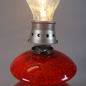 May include: A vintage table lamp featuring a red glass base with a speckled pattern and a metal fixture. The lamp is illuminated by a clear light bulb. The lamp is a decorative lighting fixture.