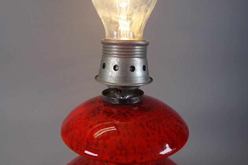 May include: A vintage table lamp featuring a red glass base with a speckled pattern and a metal fixture. The lamp is illuminated by a clear light bulb. The lamp is a decorative lighting fixture.