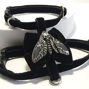 May include: Two black velvet chokers with silver-tone hardware. One choker features a silver moth pendant with a skull design. The moth pendant is attached to a black velvet bow.