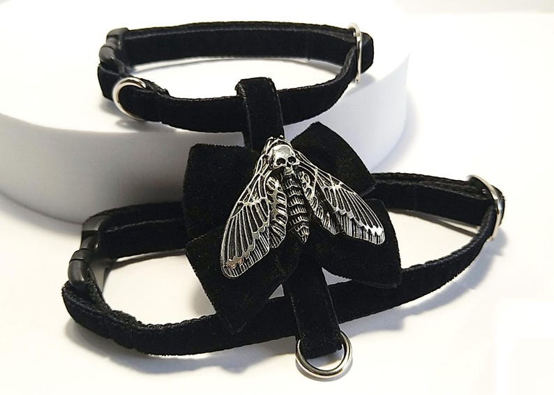 May include: Two black velvet chokers with silver-tone hardware. One choker features a silver moth pendant with a skull design. The moth pendant is attached to a black velvet bow.