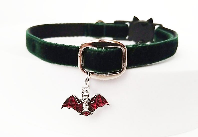 Puede incluir: Un collar para mascotas de terciopelo verde oscuro con una hebilla plateada y un dije en forma de murci&eacute;lago. El dije de murci&eacute;lago tiene alas rojas y un cuerpo plateado. El collar mide aproximadamente 1,3 cm de ancho.