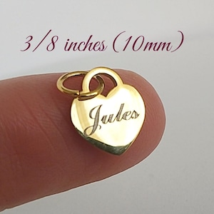 May include: A small, heart-shaped gold charm, approximately 10mm in size, with the name "Jules" engraved on the front. The charm has a small loop for attaching to a necklace or bracelet.