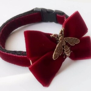 May include: A burgundy velvet pet collar with a black adjustable buckle and a burgundy velvet bow with a gold bee charm.