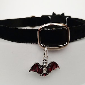 Puede incluir: Collar gargantilla de terciopelo negro con hebilla plateada y un dije de murci&eacute;lago. El dije de murci&eacute;lago tiene alas de esmalte rojo y un peque&ntilde;o acento de cristal. El collar tiene un detalle de oreja de gato.