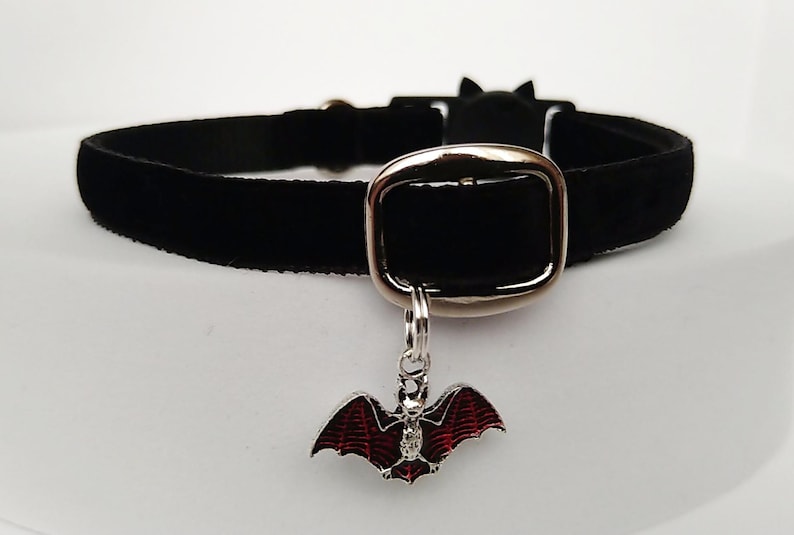 Puede incluir: Collar gargantilla de terciopelo negro con hebilla plateada y un dije de murci&eacute;lago. El dije de murci&eacute;lago tiene alas de esmalte rojo y un peque&ntilde;o acento de cristal. El collar tiene un detalle de oreja de gato.