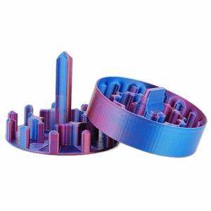 May include: Two 3D-printed objects in shades of blue and purple. One is a tall, pointed structure surrounded by smaller cylindrical shapes. The other is a ring-shaped object with a textured interior. Both objects have a gradient color effect.