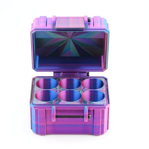 May include: A multi-colored, open container with six circular compartments. The container is a mix of purple, blue, and green hues, with a geometric pattern on the inside of the lid. The container is designed to hold small items.