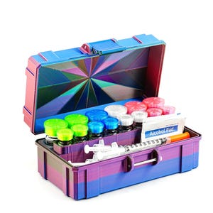 May include: A multi-colored, open medical kit with various vials, syringes, and an alcohol pad. The kit is blue, pink, and purple with a geometric design on the inside lid. The kit contains green, blue, red, and white capped vials.
