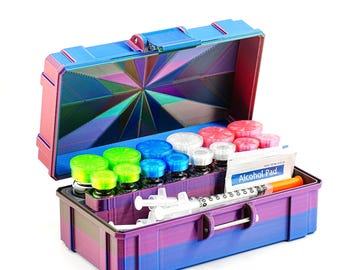May include: A multi-colored, open medical kit with various vials, syringes, and an alcohol pad. The kit is blue, pink, and purple with a geometric design on the inside lid. The kit contains green, blue, red, and white capped vials.