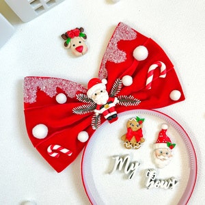 May include: A festive red bow with white accents, adorned with Christmas-themed embellishments. Includes a Santa Claus figure, candy canes, and a reindeer. A headband with the words "My bows" and gingerbread man is also present.