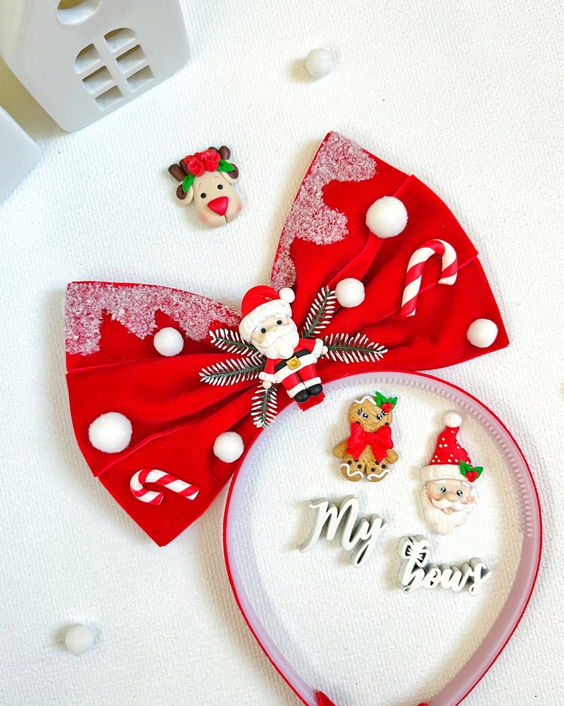 May include: A festive red bow with white accents, adorned with Christmas-themed embellishments. Includes a Santa Claus figure, candy canes, and a reindeer. A headband with the words "My bows" and gingerbread man is also present.