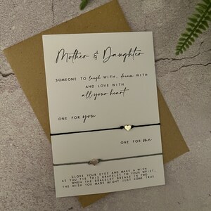 May include: A white card with black text that reads "Mother & Daughter Someone to laugh with, dream with and love with all your heart One for you One for the Close your eyes and make a wish as you tie this bracelet to your wrist. When the bracelet breaks in two the wish you made might just come true."