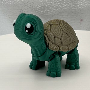 May include: A small green and brown turtle figurine with large eyes. The turtle has a detailed shell and is posed walking.