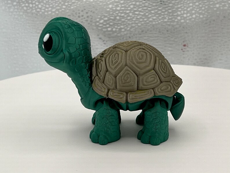 Puede incluir: Una tortuga de juguete de pl&aacute;stico verde y marr&oacute;n con un caparaz&oacute;n detallado y ojos grandes.