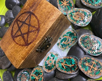 May include: A wooden box with a pentagram design on the lid, surrounded by small, round, clear glass stones with green and gold accents. Each stone features a different symbol.