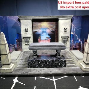 Könnte beinhalten: Ein Diorama-Präsentationssockel mit einem zentralen steinartigen Altar auf einem schwarz-weiß marmorierten Podest, flankiert von zwei Obelisken. Der Hintergrund zeigt eine Stadtkulisse mit Blitzen und einer Pyramide. Der Text lautet: US import fees paid at origin. No extra cost upon arrival.