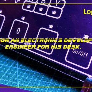 May include: A black acrylic panel featuring white printed labels including Logic Gates, Mode, 0, 1, and On/Off, with a white line drawing of a cat. The text A GIFT FOR AN ELECTRONICS DEVELOPMENT ENGINEER FOR HIS DESK is printed across the centre.