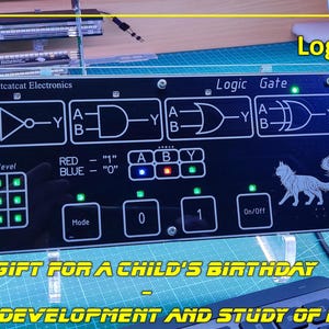 May include: A black rectangular electronic logic gate training board with white printed circuit diagrams, including NOT, AND, OR, and XOR symbols. The device features labelled buttons for Mode, 0, 1, and On/Off, with small LED indicators and a cat graphic.