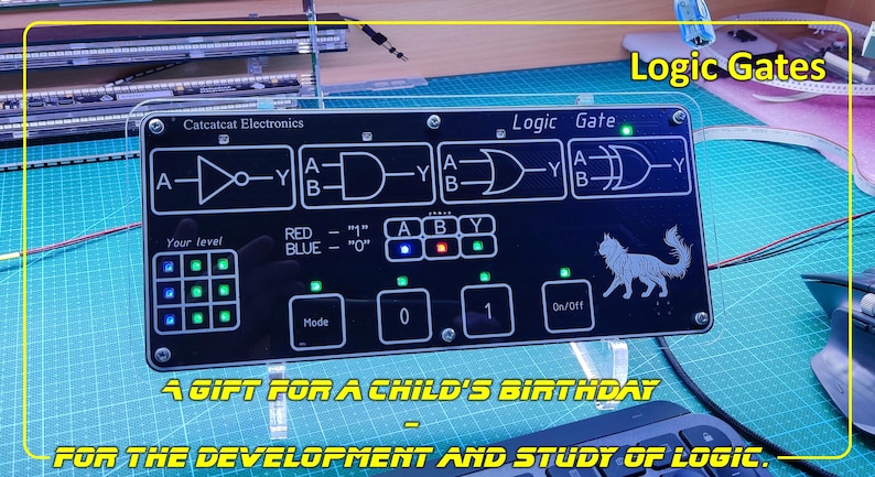 May include: A black rectangular electronic logic gate training board with white printed circuit diagrams, including NOT, AND, OR, and XOR symbols. The device features labelled buttons for Mode, 0, 1, and On/Off, with small LED indicators and a cat graphic.