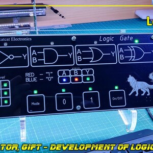 May include: A black rectangular electronic logic gate simulator board with white printed circuit diagrams, including NOT, AND, OR, and XOR symbols. The device features a grid of green LED indicators, a cat graphic, and buttons labelled Mode, 0, 1, and On/Off.