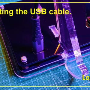 May include: A black acrylic logic gate circuit board with a USB cable connected to a port. The device features clear acrylic supports and silver hardware. The text "Connecting the USB cable." and "Logic Gates" is printed on the image.