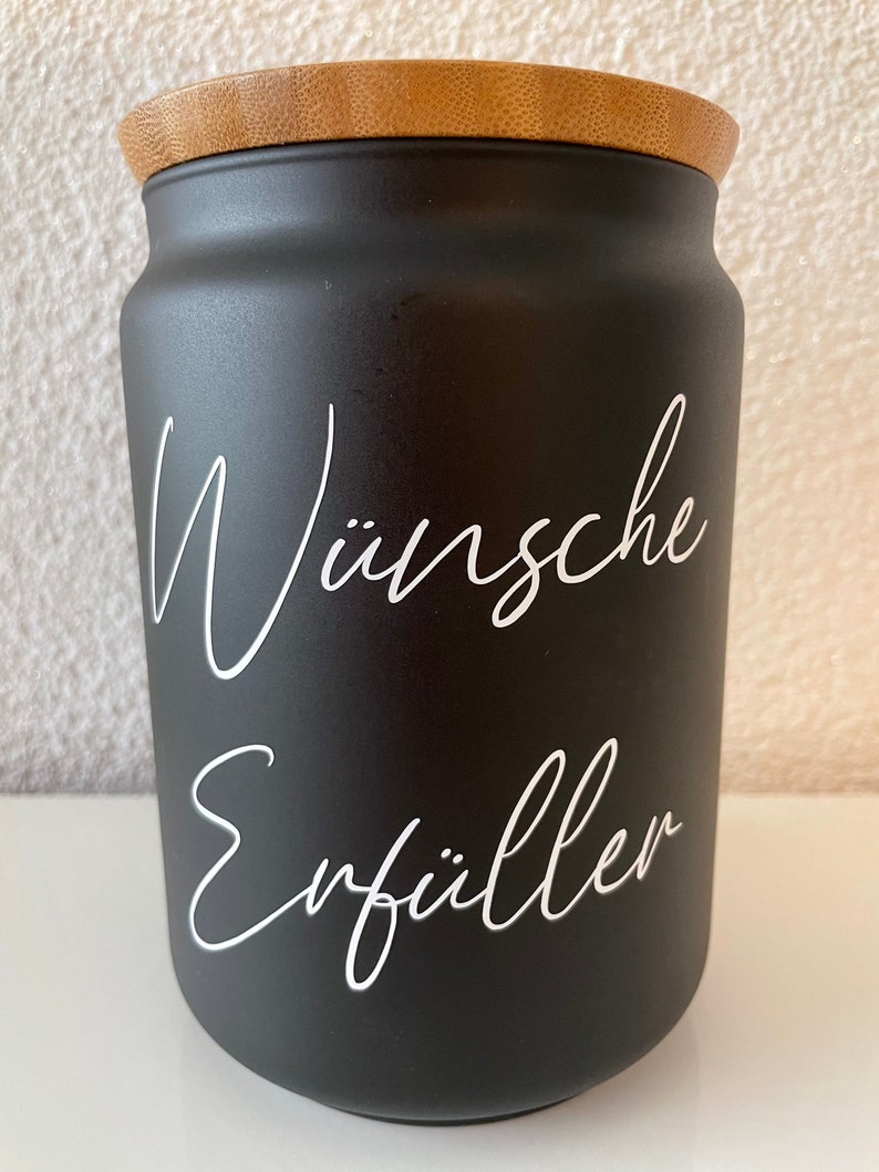 May include: Black ceramic jar with a bamboo lid. The jar has white lettering that says "W&uuml;nsche Erf&uuml;ller".