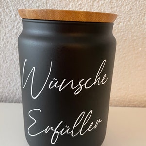 May include: Black ceramic jar with a wooden lid. The jar has white lettering that says "W&uuml;nsche Erf&uuml;ller".