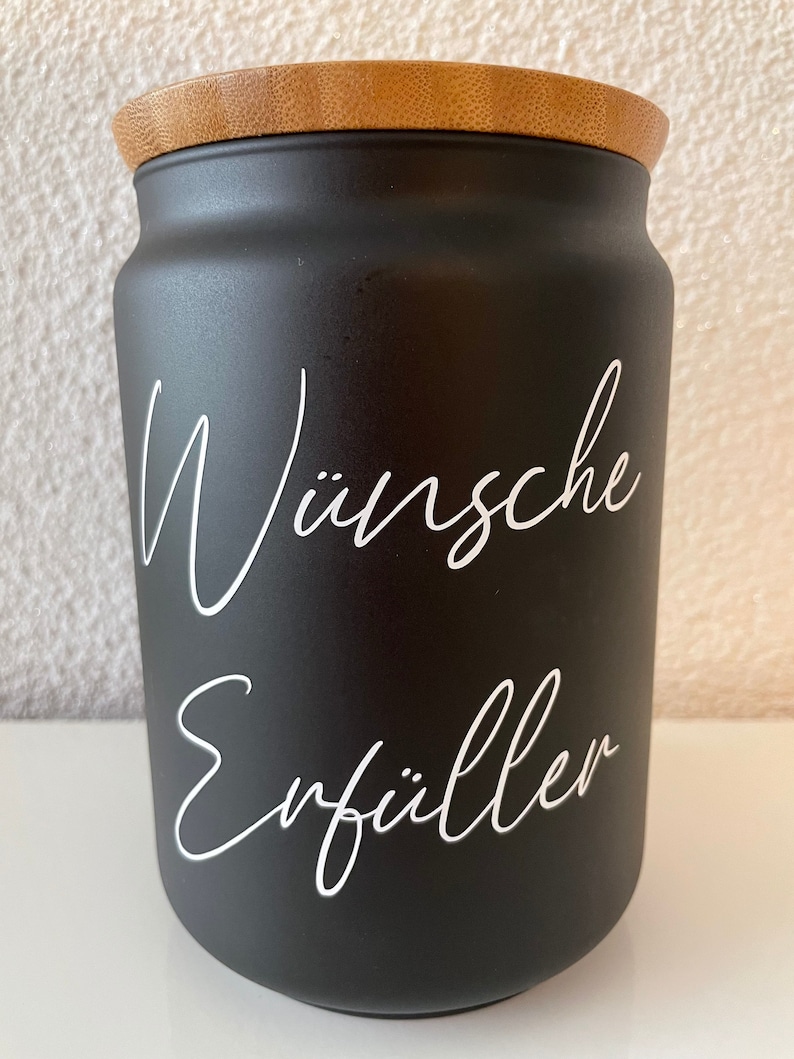 May include: Black jar with a bamboo lid and white lettering that says "W&uuml;nsche Erf&uuml;ller".