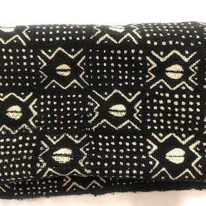 May include: Folded black fabric with a repeating pattern of cream-colored geometric shapes and dots. The design features stylized eye-like shapes within a diamond and zig-zag pattern. The fabric appears to be soft and textured.